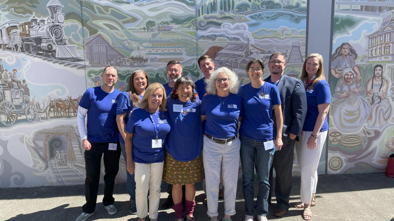 10 people in front of mural with blue shirts.