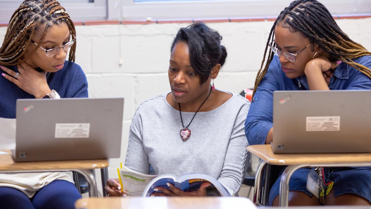 3 teachers talking with book and computers